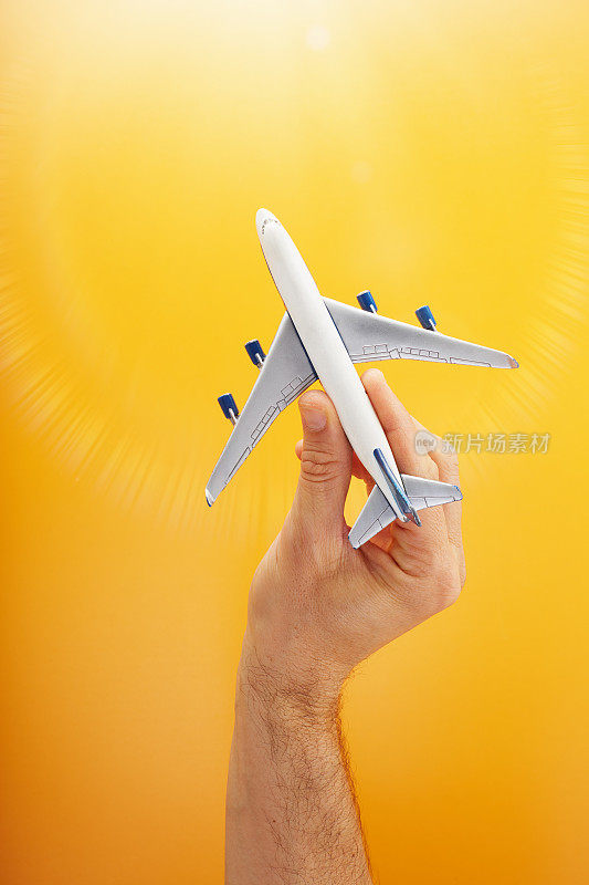 Hand holding a model airplane against warm orange background with a nice sun flare at the top of the frame